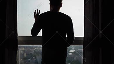 Silhouette of man walking to window and looking out
