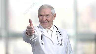 Senior old doctor in white coat and stethoscope shows thumb up.