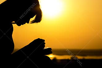 Silhouette of the hands of woman praying to God in the nature witth the Bible at sunset, the concept of religion and spirituality
