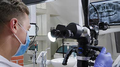 Men specialist works with optical microscope in front of jaw on monitor in dentist`s office