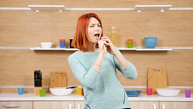 Woman with a wooden spoon in hands sings at the kitchen