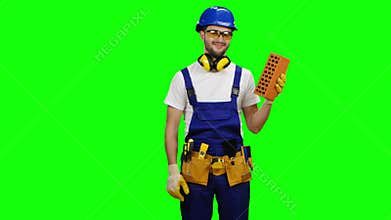 Engineer holds a brick in his hand and shows a thumbs up. Green screen