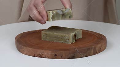 A close-up of woman`s hands putting bars of natural lavender soap on a round wooden tray. On the top she puts two bars