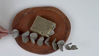 A round wooden board with a bar of lavender eucalyptus soap and a twig in front of it.