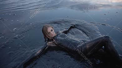 Adorable Slender Blonde Lays Smeared in a Black Mud looks like Petroleum Oil