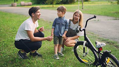 Loving parents are making surprise for little son closing his eyes and giving him new bicycle as present, happy boy is