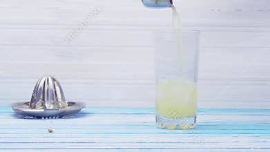 Making Lemonade With Freshly Squeezed Organic Lemons Dropping Ice Cubes In Glass Cup And Mixing With Water