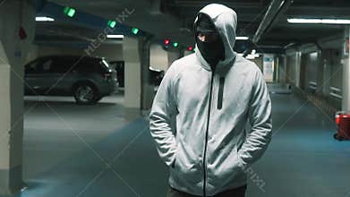 Man criminal in black balaclava and hood walks and looks around menacingly.Slow mo