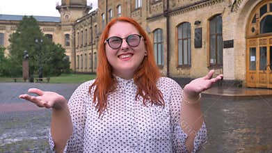 Fat ginger girl with glasses is walking in park under rain, raising hands, excited about rain, inspiration concept