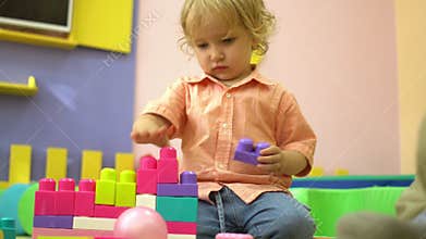 Beautiful blonde preschool cute toddler playing with multi coloured building blocks in kindergarten. Child development