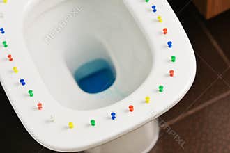 Conceptual image of a hemorrhoid disease with multi-colored thumbtacks on toilet bowl cover