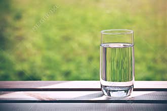 Glass of pure water on green natural background