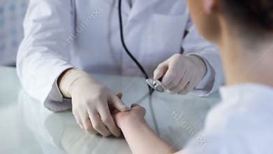 Doctor listening to pulse of woman with stethoscope, appointment at clinic