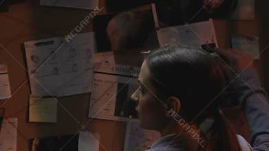 Female police officer searching for solution crime ideas on investigation board