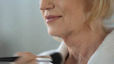 Mature woman applying face powder by make-up brush, preparing for date, beauty
