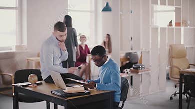 Two casual multiethnic colleagues collaborate in modern healthy workplace, Caucasian confident female boss walking by.