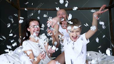Kid with parents throw artificial snowflakes and have fun time sitting on bed in bedroom