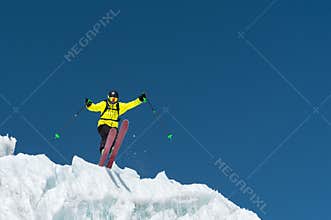 A jumping skier jumping from a glacier against a blue sky high in the mountains. Professional skiing
