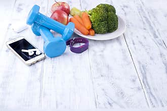 Sports equipment, blue dumbbells and fruits, vegetables and telephone. Fitness bracelet and headphones for music. Free space for