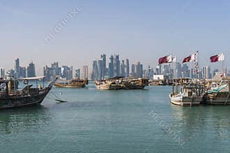 DOHA, QATAR - Feb 2018: Beautiful Doha Skyline View with Traditional Wooden Boats with Floating Qatar Flags. Corniche