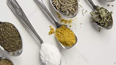 Camera moves along of spoons with various aromatic herbs and spices on white background