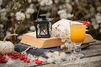 Still life. Old books and sea buckthorn tea in a transparent glass among fluffy dry autumn colors. Atmosphere of relaxation and tr