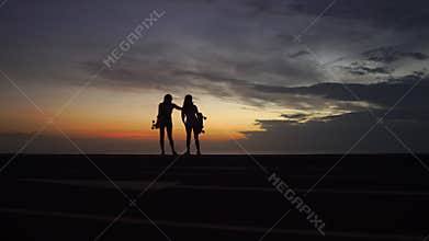 Girlfriends look at the beautiful view of the sunset sky after skateboarding on top of the mountain