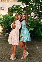 Slender ladies with long wavy hair holding stylish straw bags.