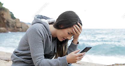 Sad girl receiving bad news online on the beach