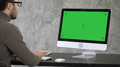 Elegant businessman analyzing data in office on his computer. Back view to the monitor. Green Screen Mock-up Display.