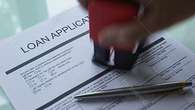 Loan application document rejected, hand stamping seal on official paper closeup
