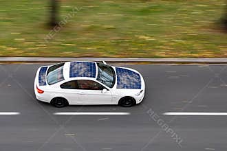 Very quickly driving white ecological solar electric car on a city street. The image is taken with a strong motion blur effect