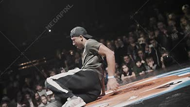 Attractive sporty guy in grey t-shirt and cap dynamically breakdancing on stage