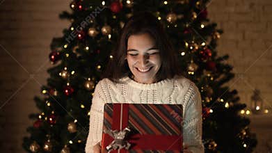 The girl makes a wish and opens a Christmas gift package. the concept of holidays and New year. the girl is happy and