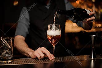Bartender adds sparkling wine in cocktail on a bar counter