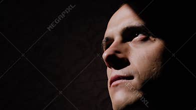 The young man`s face slowly emerges from the shadows into the light. Very cinematic shot. Beautiful shadows on his face.