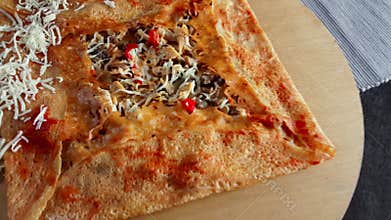 Delicious crepe with mushroom and cheese served with seasonings on a wooden board