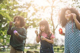 Group of Diverse Kids cute friends having bubble fun on green lawn in park.