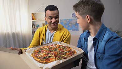 Two multiracial friends opening box with pizza for student party, food delivery
