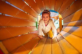 Happy child girl playing in tunnel on playground