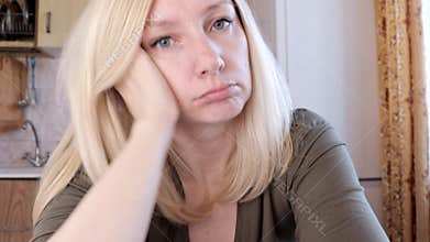 Portrait of a sad and bored young blond woman sitting in kitchen, sadness and depression concept