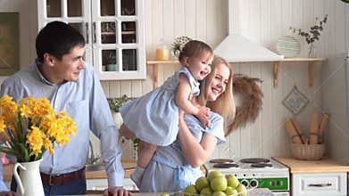 Happy family in the kitchen, where the mother holds her daughter, and dad is standing nearby.