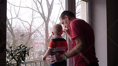 An old man and his adorable little grandson are playing by the window and grandfather show to the baby boy a bird on the