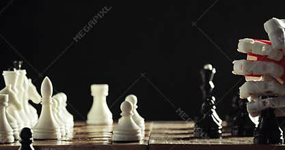 Robotic hand prosthesis is playing chess with human hand on black background.