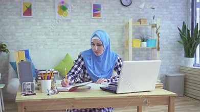 Beautiful young muslim woman in hijab, studying in modern apartments