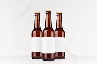 Three brown longneck beer bottles 330ml with blank white label on white wooden board, mock up.