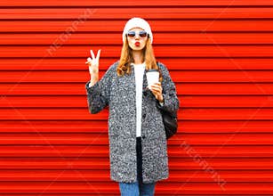 Fashion pretty woman with coffee cup in coat posing on red