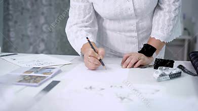 Close up of female hands with pin cushion and pencil drawing outline. Image of body of a woman in white blouse and skirt