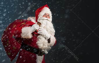 Santa Claus holding a bag with presents and ringing a bell on a dark background