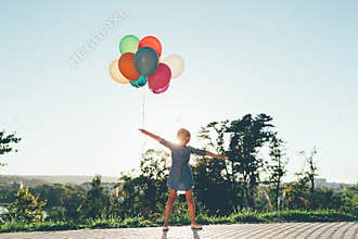 Cute girl holding colorful balloons in the city park dreaming